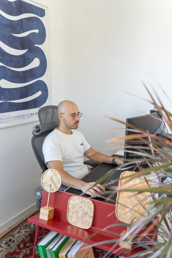 Francesco Nocentini al lavoro alla scrivania, ripreso oltre le foglie di una pianta