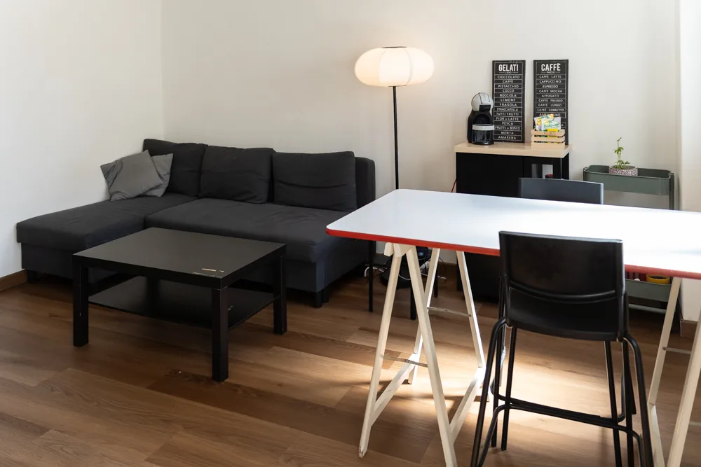 La lounge di Le Mura 85 con divano grigio, tavolino e tavolo alto da lavoro