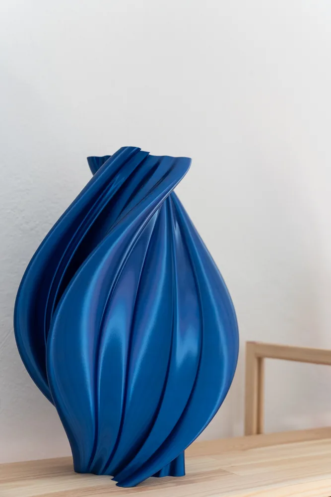Dettaglio di un vaso blu a spirale stampato in 3D, appoggiato alla mensola