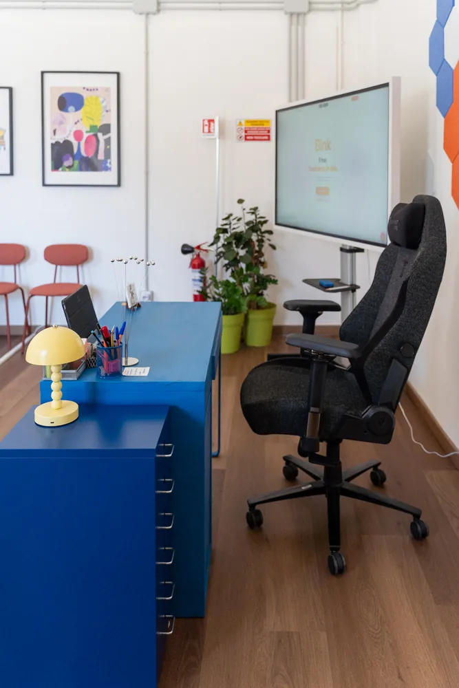 La postazione di lavoro con scrivania blu e sedia operativa, in fondo alla sala