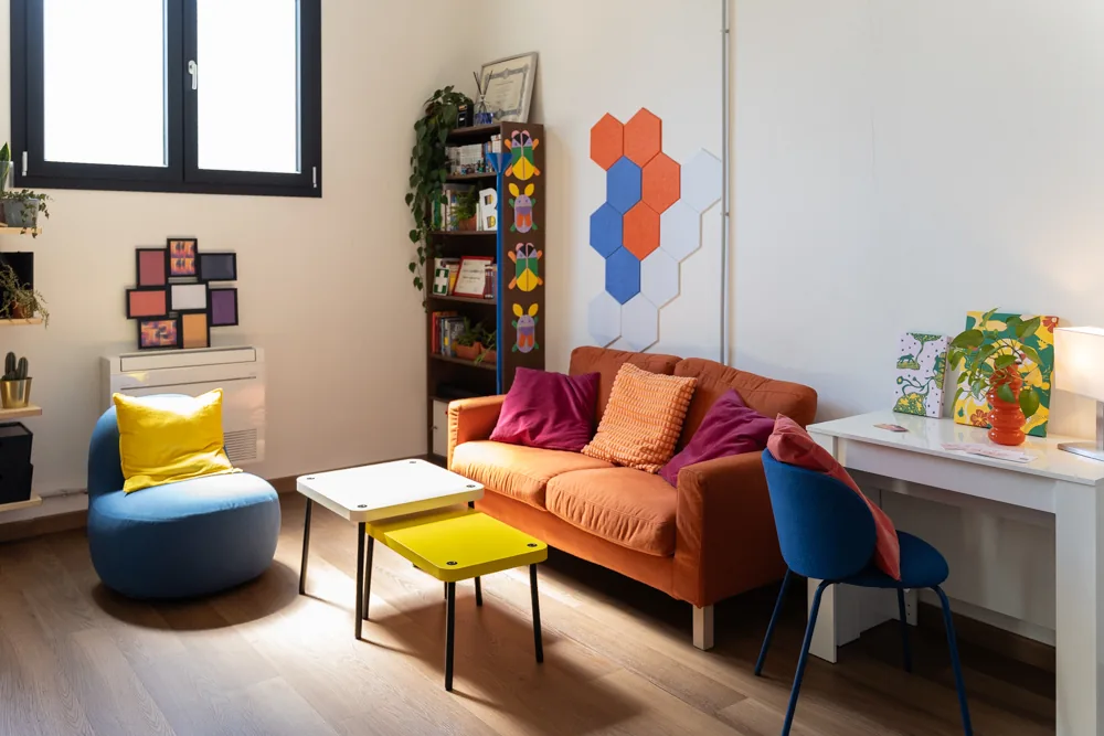 La lounge con pouf blu e tavolino giallo, vista verso la finestra