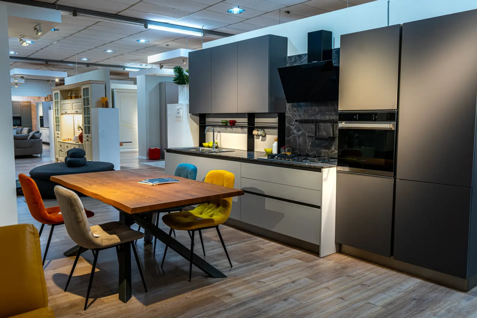 Cucina grigio scuro con tavolo in legno e sedie colorate, fotografia Koral per Londi Arredamenti